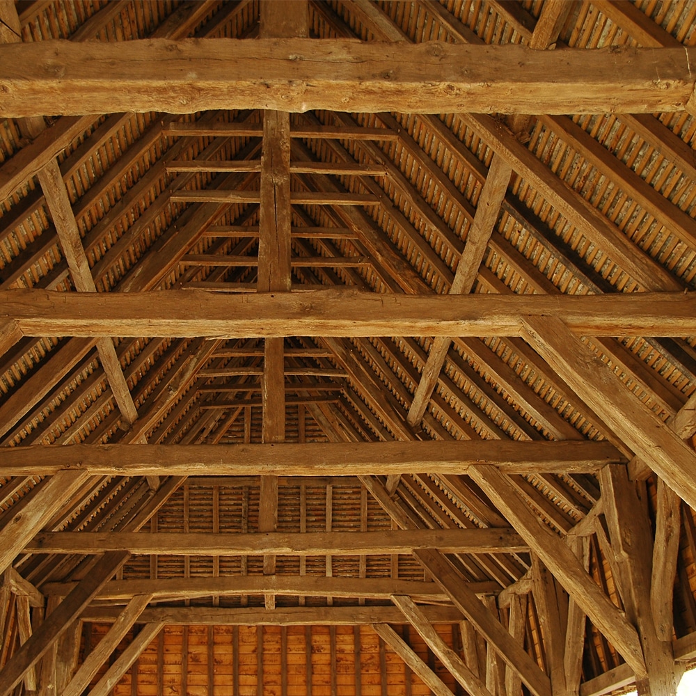 Plafond en bois d'une charpente traditionnelle, avec des poutres, chevrons et lattes formant une structure complexe et solide.