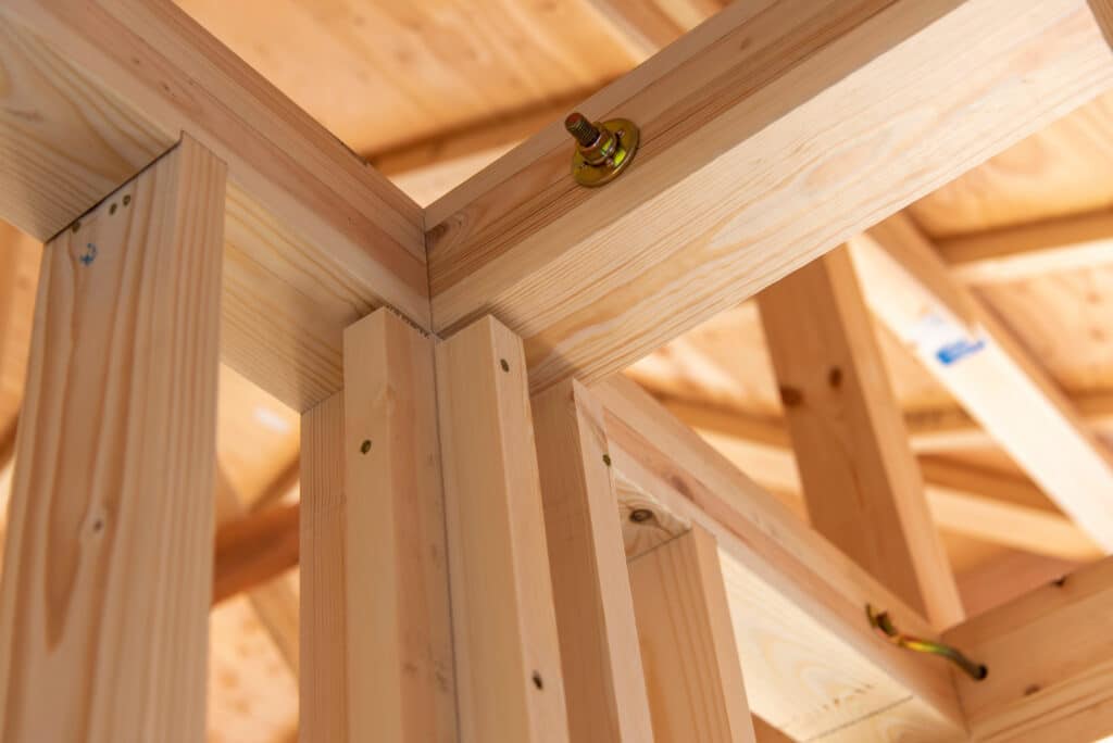 Charpente en bois neuf d'une maison en construction. Poutres et poteaux d'ossature clairs, avec boulons de fixation dorés.