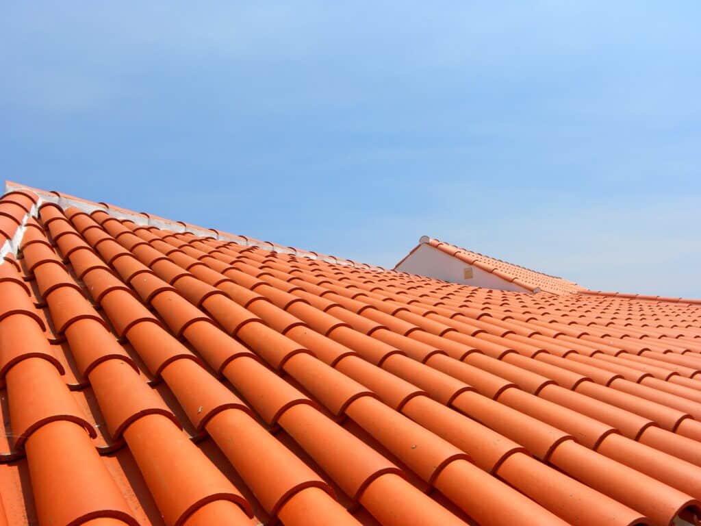 Toit en tuiles de terre cuite orangées sous un ciel bleu clair. Lignes régulières de tuiles courbées et jointures blanches.